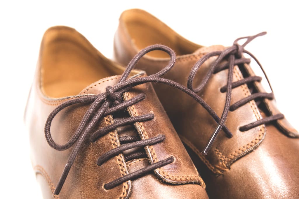 Close view of a pair of tan leather derby shoes with brown waxed laces and visible welt stitching.