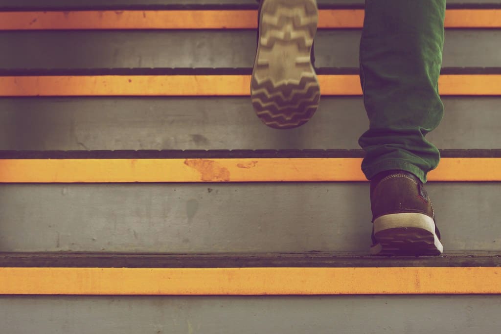 Looking down a flight of stairs with yellow edge strips as a rubber-soled boot lifts off the step above.