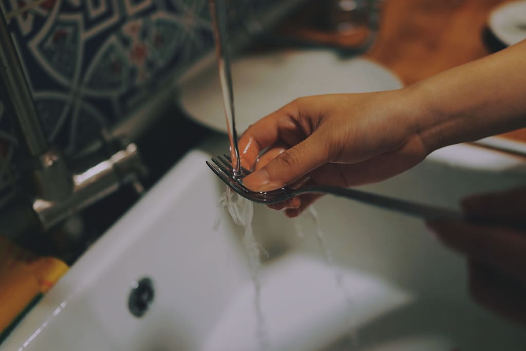 A hand under a running faucet over a white sink, water splashing off the fingers.