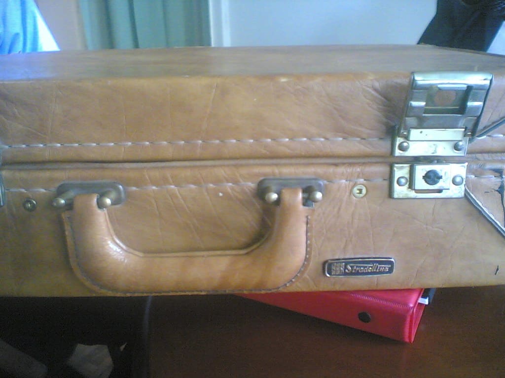 Close view of the handle and brass latches of a tan leather briefcase.
