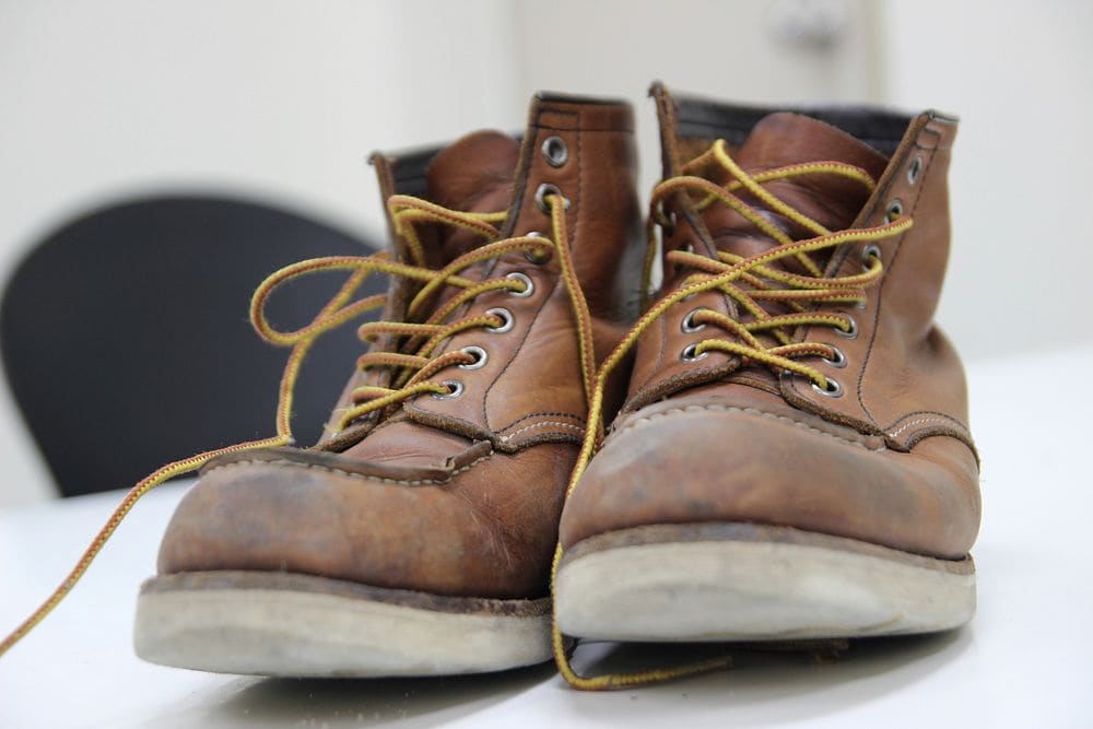 A pair of worn tan leather lace-up work boots with yellow laces and visible welt stitching.